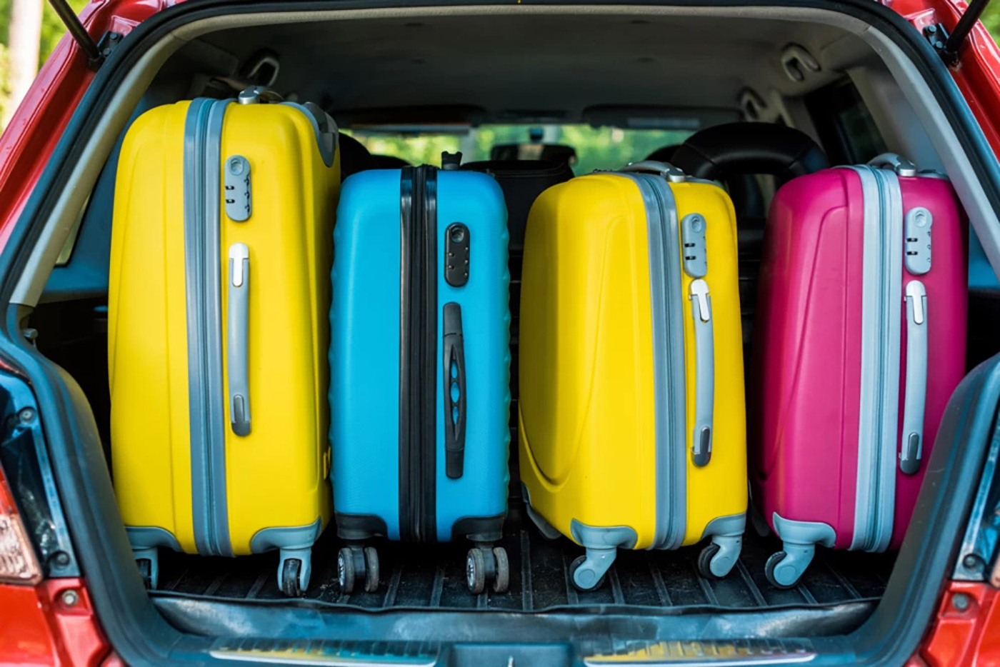 Two bright yellow suitcases, a bright blue suitcase and a bright pink suitcase in the back of a red SUV with the hatch open.