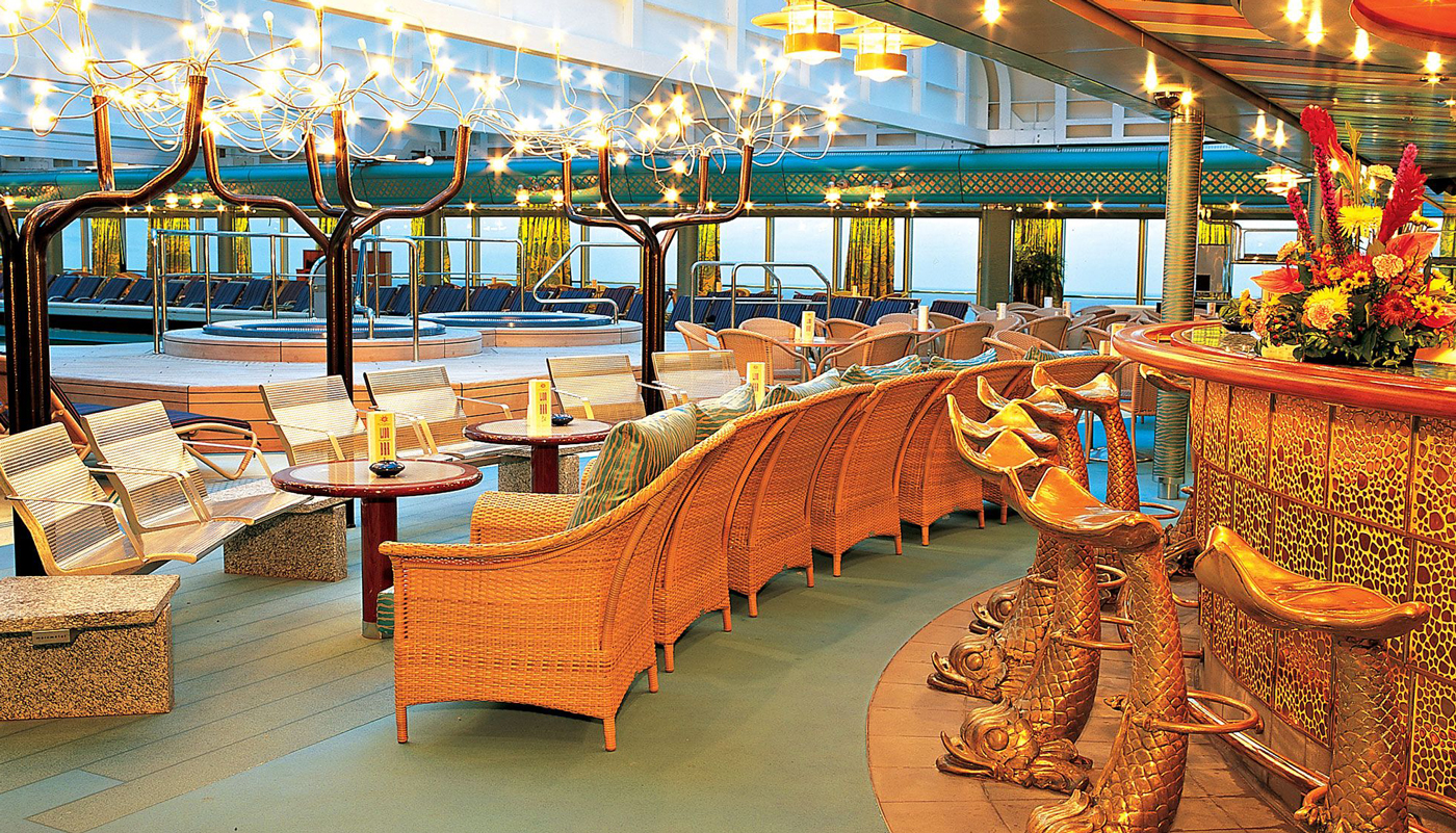 The poolside lounge on a Holland America ship featuring a cocktail bar, comfortable seating and unique golden fish bar stools.
