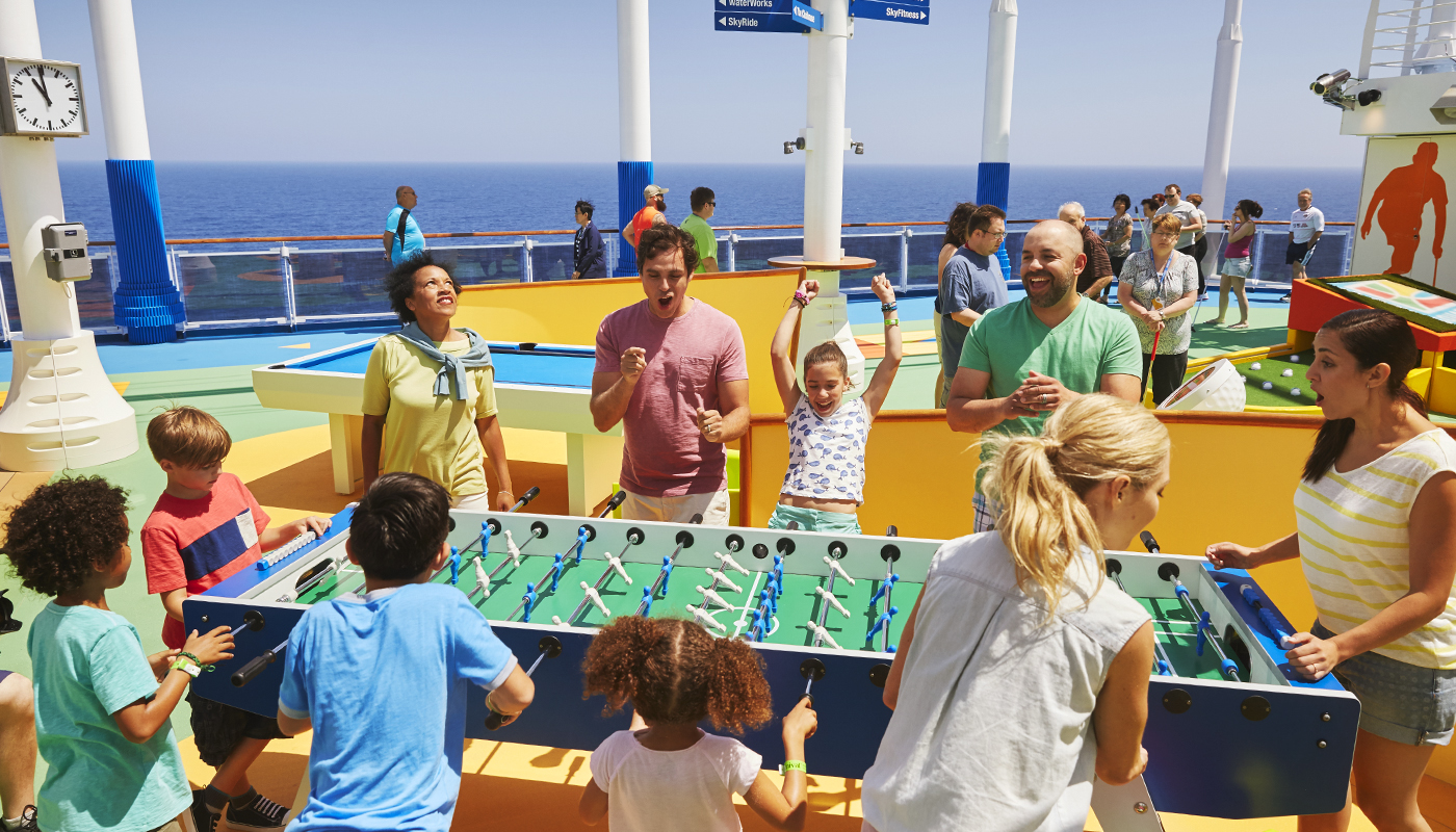 Multigenerational family playing game of Foosball on cruise ship top deck